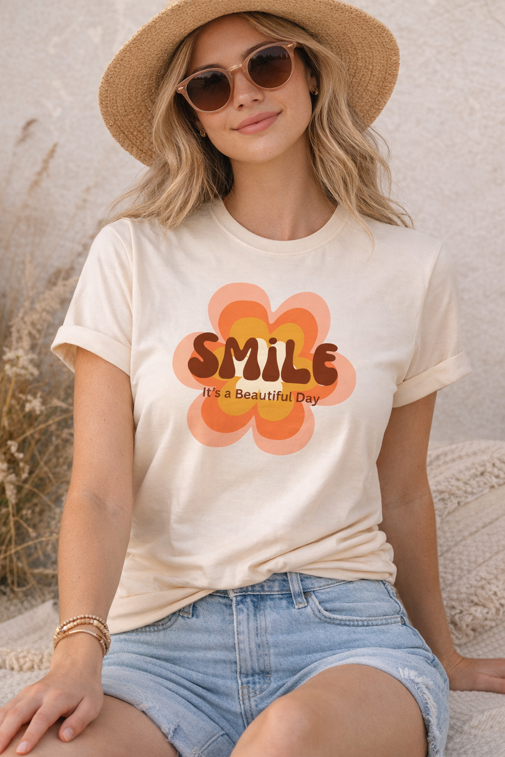 Lady on beach wearing Retro smile flower t-shirt with “It’s a Beautiful Day” groovy 70s design on cream Bella Canvas shirt