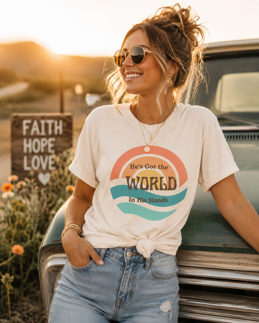 Woman wearing He's Got the Whole World Vintage Soul Tee featuring a retro sunset graphic and faith-inspired message on a Bella + Canvas shirt