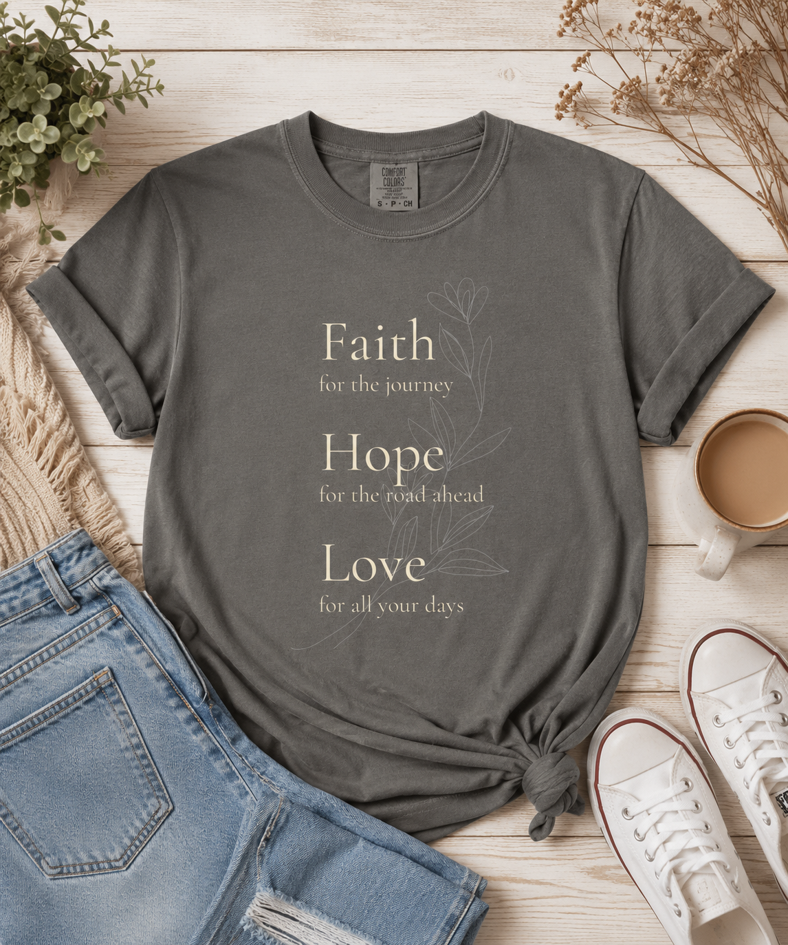 Graphite Comfort Colors t-shirt featuring a Faith Hope Love floral design styled in a warm flat lay with denim jeans, white sneakers, a coffee mug, and neutral home accents. Vintage-inspired artwork with a timeless, uplifting aesthetic.