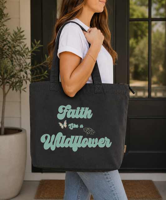Woman carrying a graphite Comfort Colors Everyday Zip Tote featuring the Faith Like a Wildflower design in soft teal and floral details. Inspirational faith-inspired tote with a vintage-inspired aesthetic for everyday use.