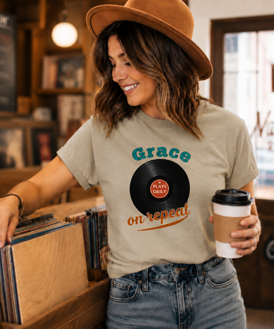 Vintage-inspired Comfort Colors Sandstone t-shirt featuring a retro vinyl record graphic with the uplifting phrase “Grace Plays Daily on Repeat,” styled in a warm nostalgic record shop setting with cozy Americana vibes.