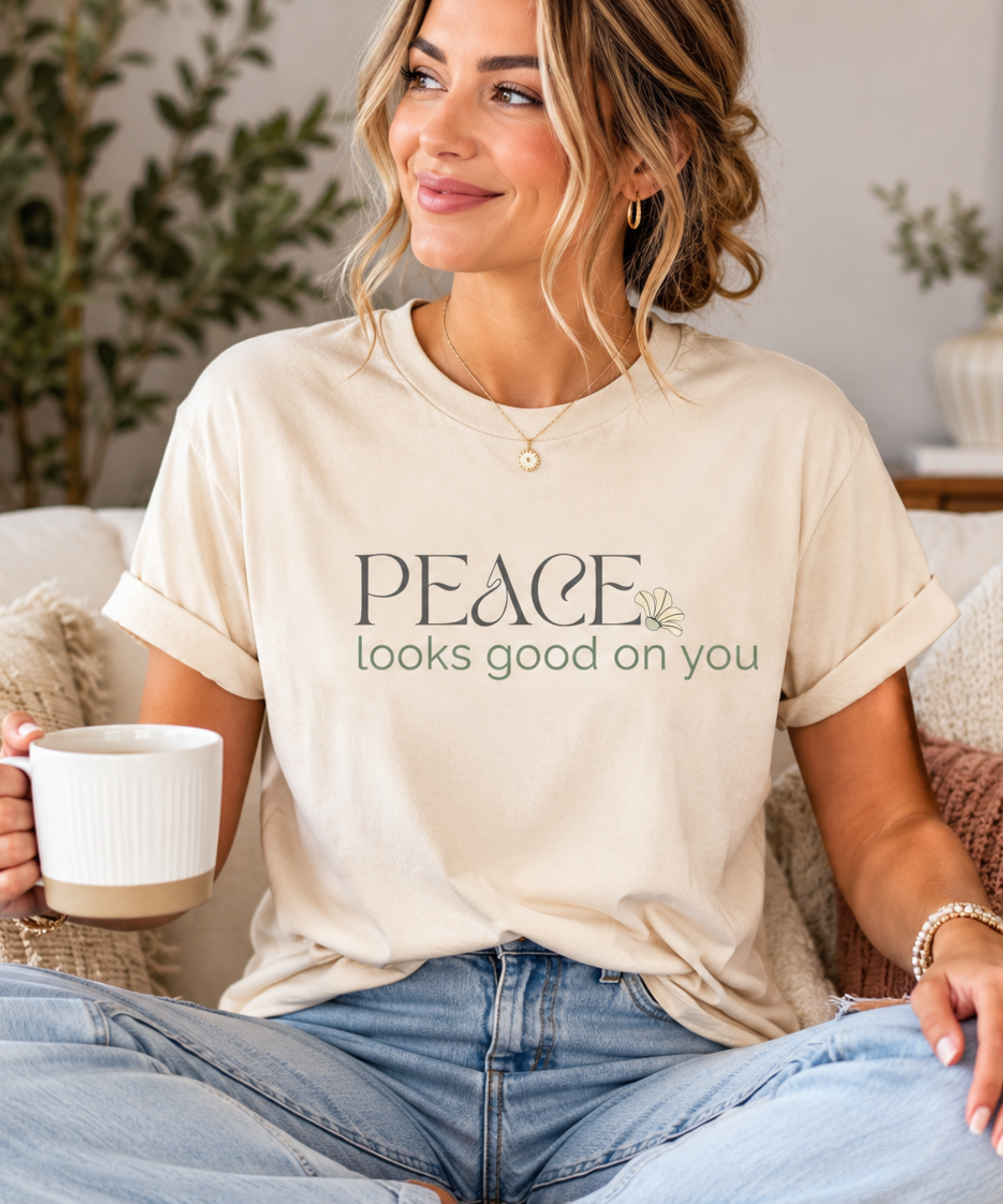 Woman wearing a cream Peace Looks Good on You vintage-inspired graphic t-shirt while relaxing on a sofa in a modern neutral living room.