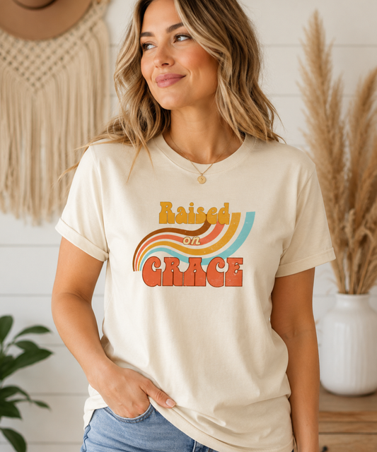Woman wearing cream Raised on Grace distressed vintage graphic tee featuring retro typography and a worn-in nostalgic design on a Bella + Canvas shirt