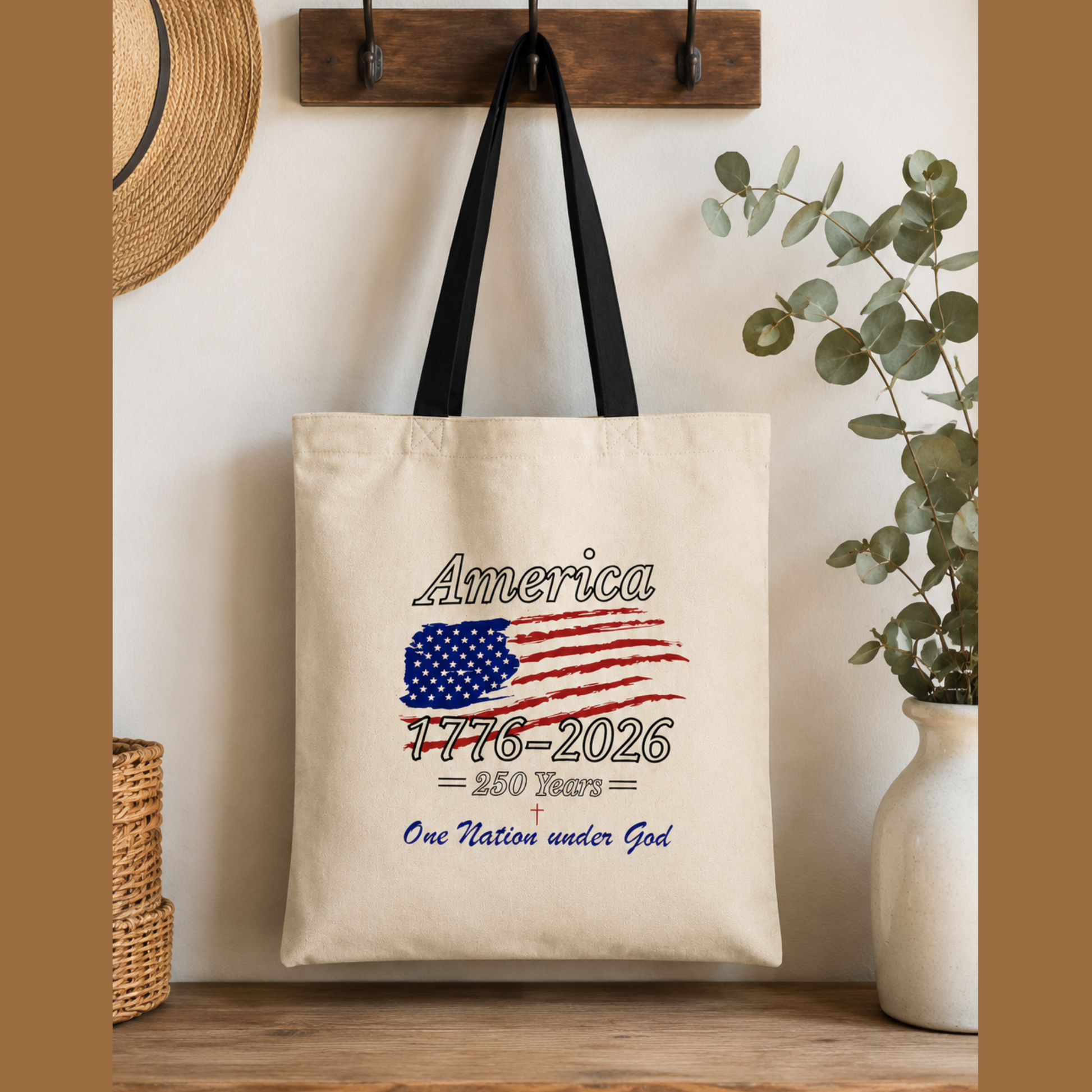 Canvas patriotic tote bag hanging on wooden wall hook featuring America 1776-2026 and One Nation Under God design